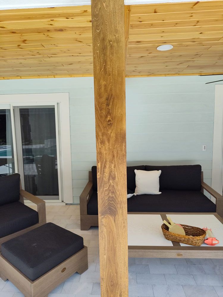 Covered patio with dark outdoor seating, white siding, and a central wooden post.