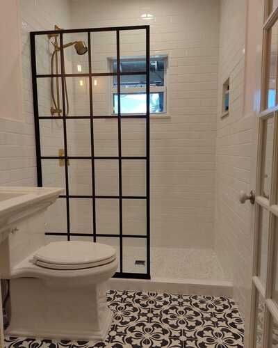 Small bathroom with toilet, glass shower panel, white tile walls, and black-and-white patterned floor.