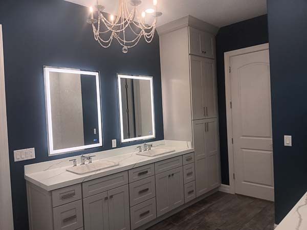 Modern bathroom with navy walls, double vanity, lit mirrors, and a chandelier