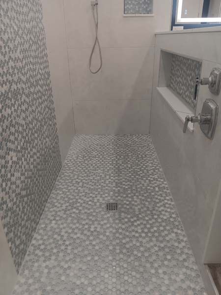 Small tiled shower stall with gray mosaic floor, wall tiles, and chrome fixtures.