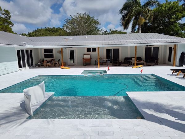 Modern white villa patio with turquoise swimming pool and palm trees in bright sunlight