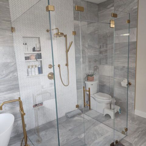 Modern marble bathroom with glass shower, gold fixtures, toilet, and white step stool