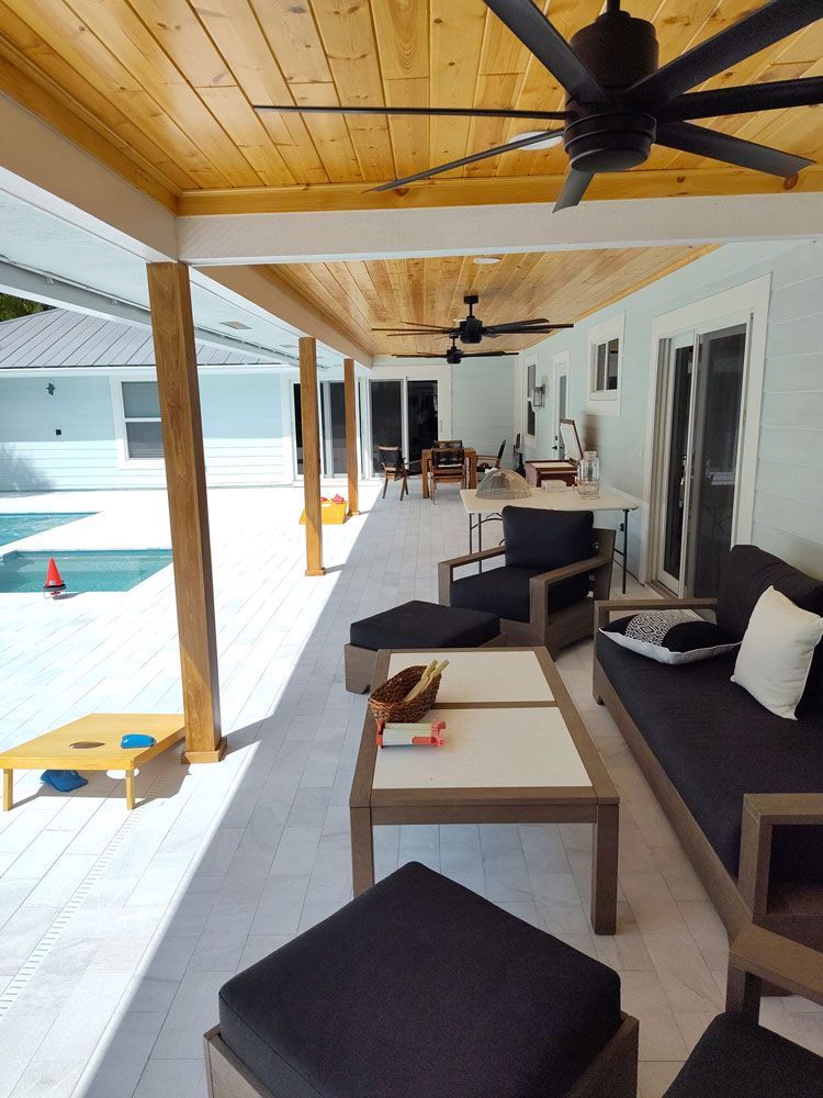 Covered patio with wood ceiling, ceiling fan, lounge chairs, and poolside view