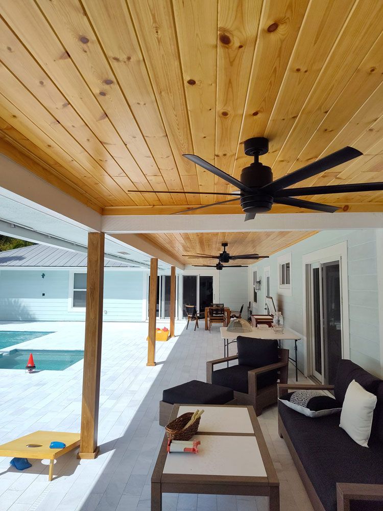 Covered patio with ceiling fans, wicker seating, and ocean view beside a pool