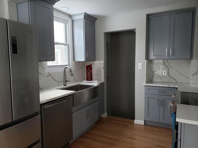 Modern kitchen with stainless steel appliances, gray cabinets, white countertops, and wood floors