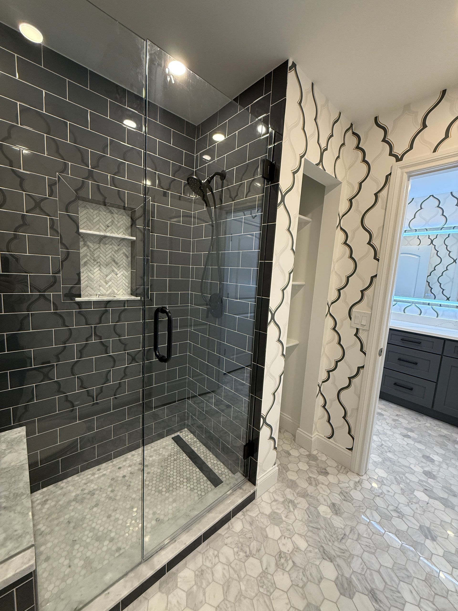 Modern bathroom with black-tiled glass shower, hexagon floor, and white patterned walls