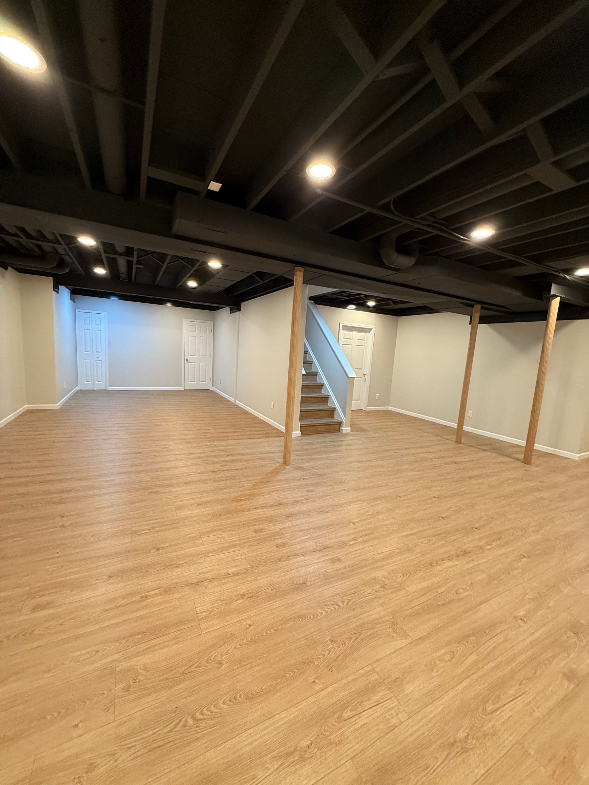 Empty indoor studio space with wood floor, white walls, and black exposed ceiling beams
