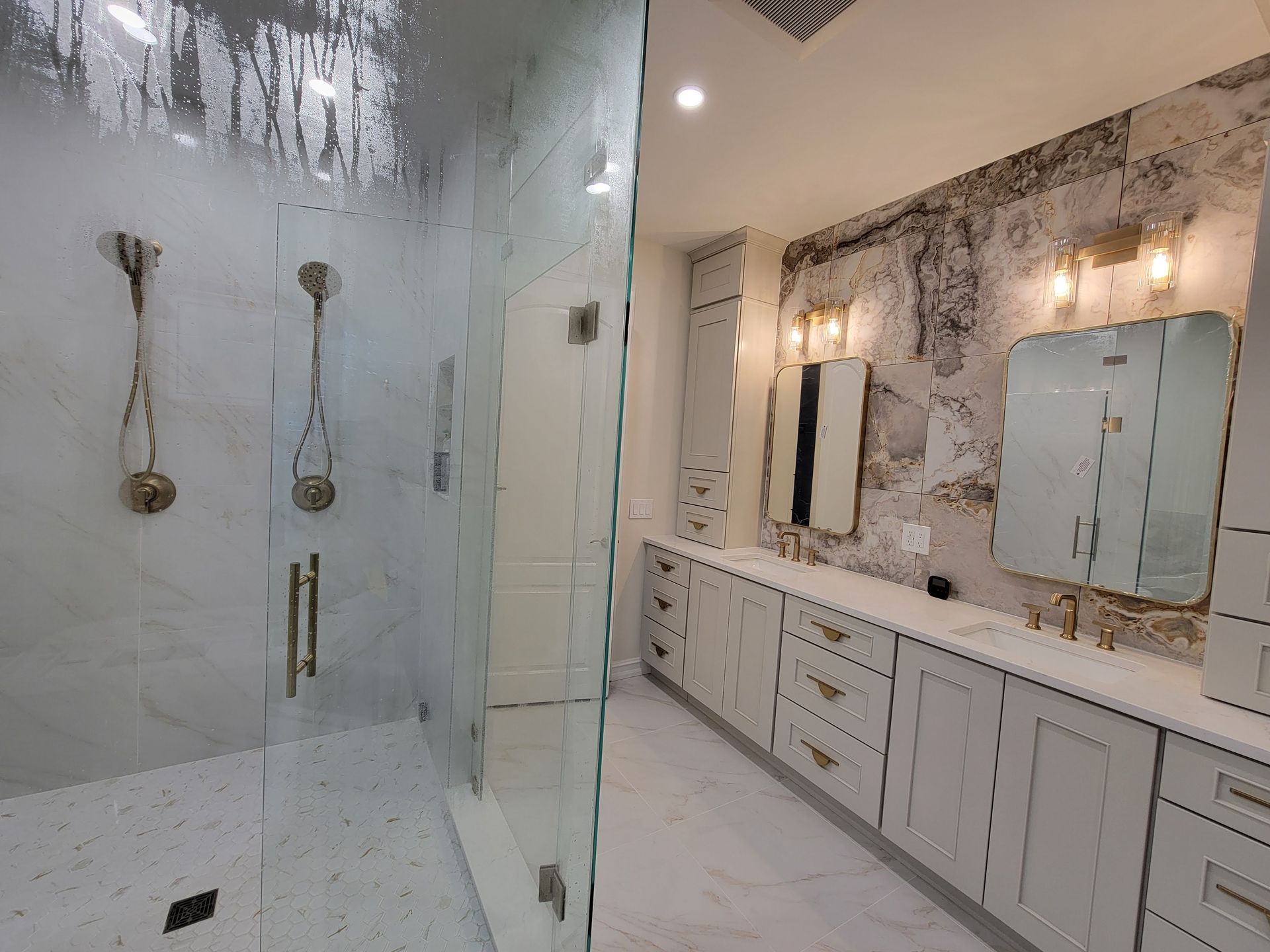 Luxury bathroom with glass shower, marble walls, and white double vanity with mirrors and sconces