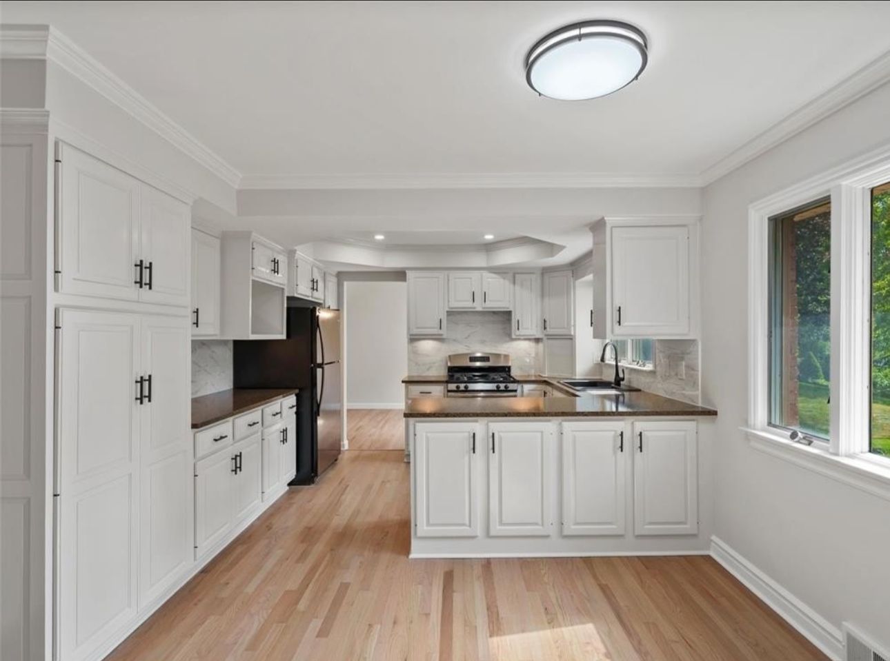 Bright modern kitchen with white cabinets, wood floors, stainless appliances, and a central island.