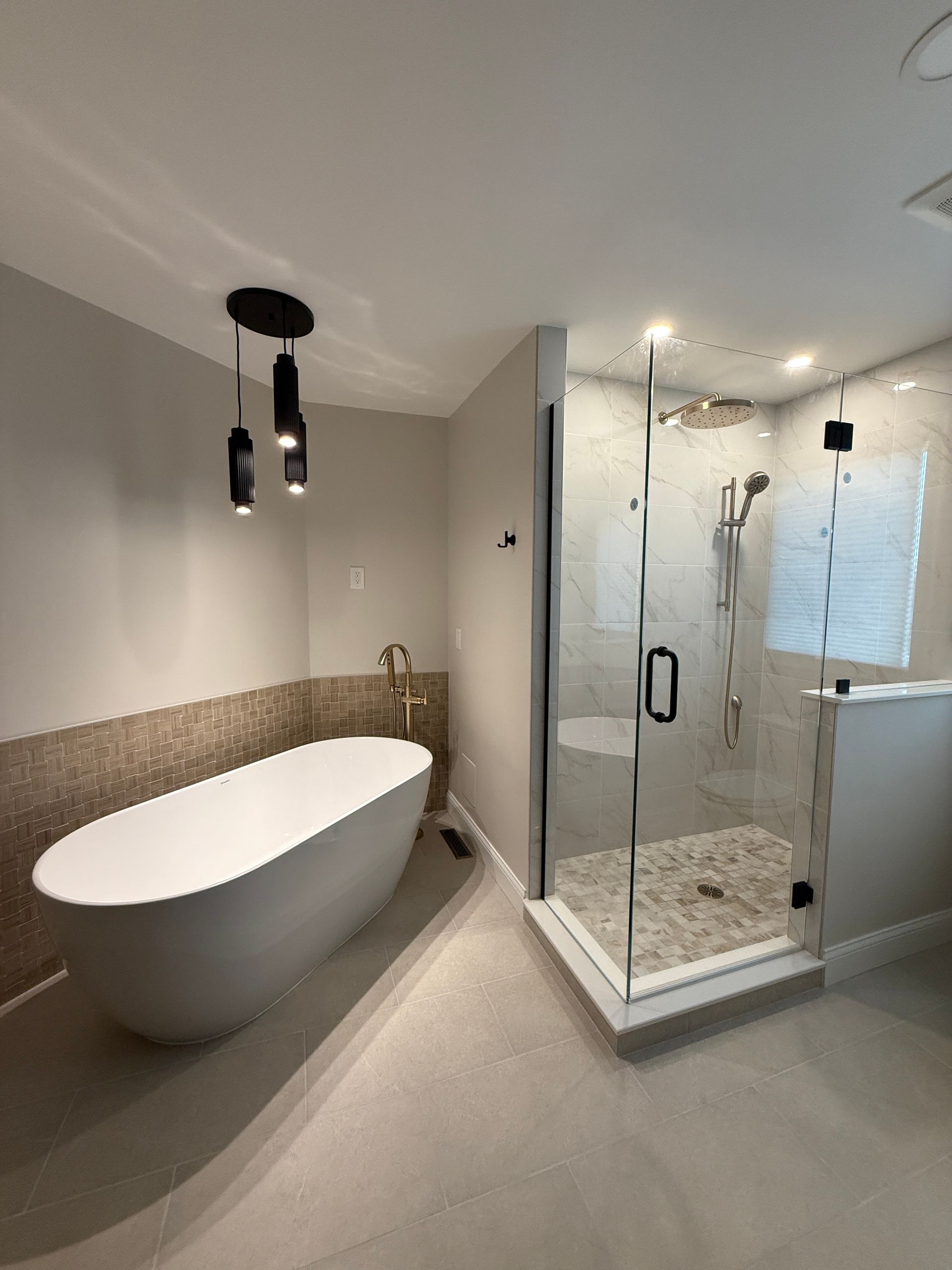 Modern bathroom with freestanding tub, glass shower, beige tile, and pendant lights