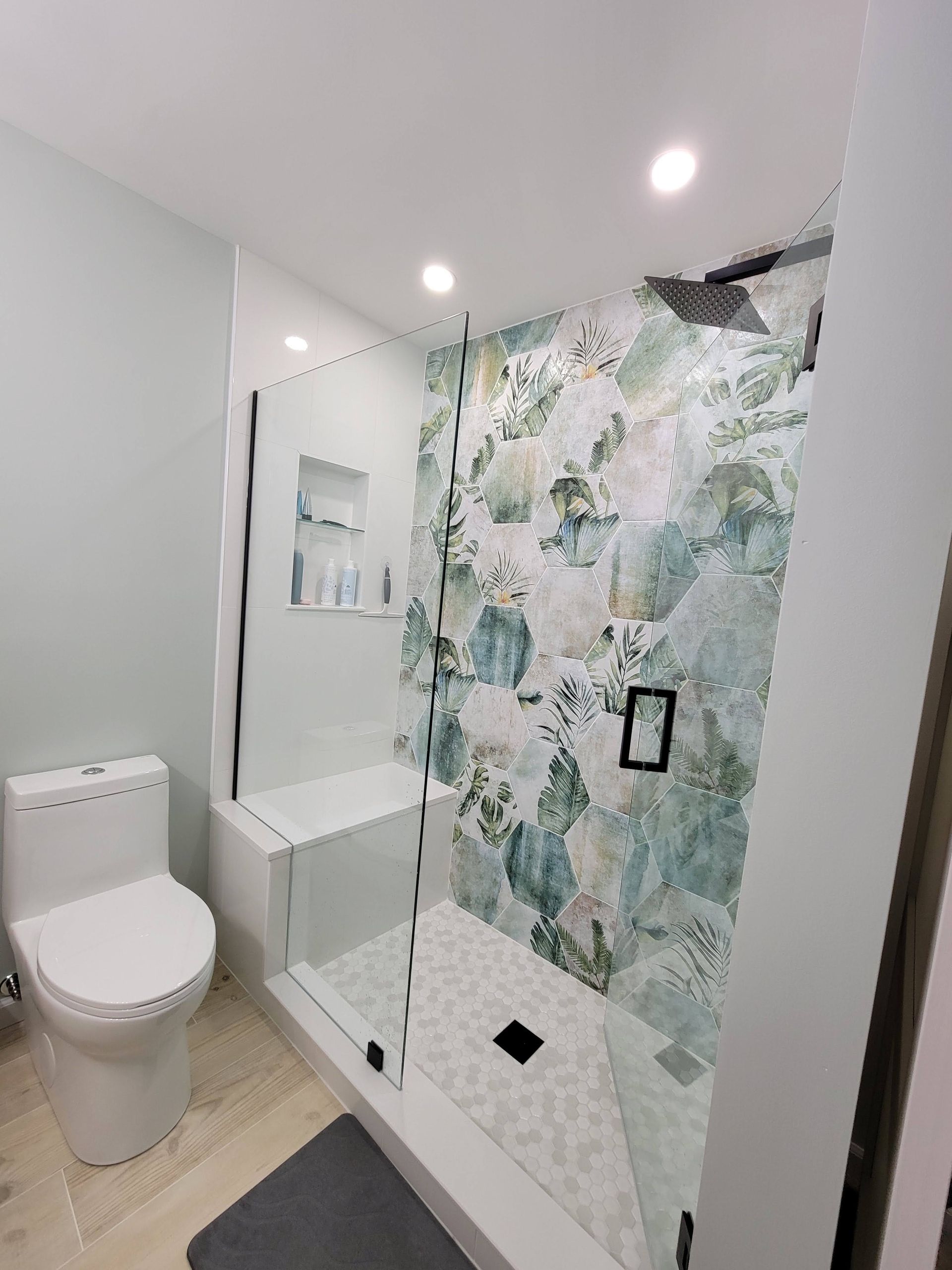 Modern bathroom with white toilet and sink, glass shower, and green floral tile accent wall