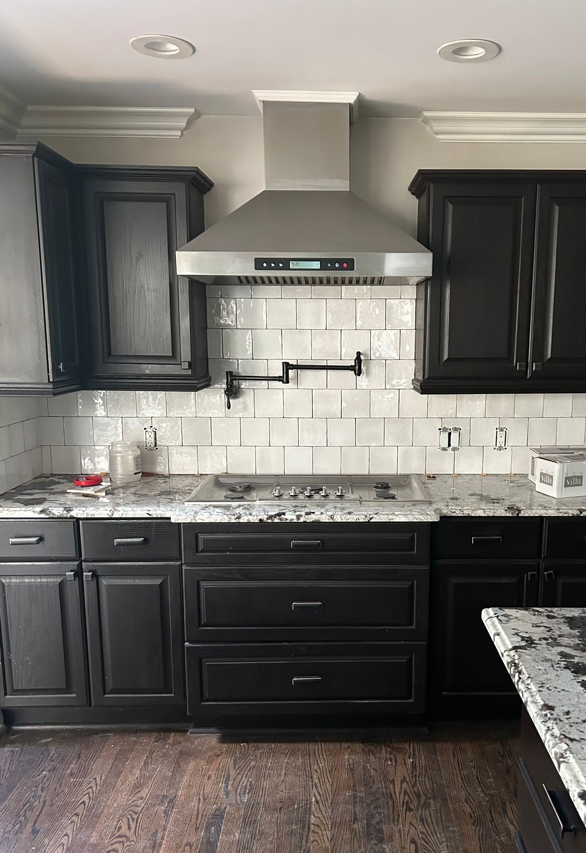 Modern kitchen with dark cabinets, white subway tile backsplash, stainless range hood, and granite counters