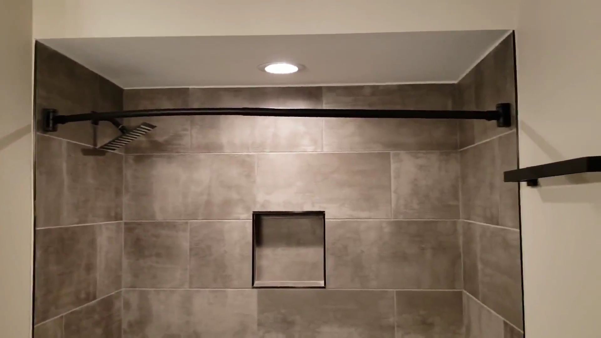 Empty tiled shower with a shower curtain rod and recessed ceiling light