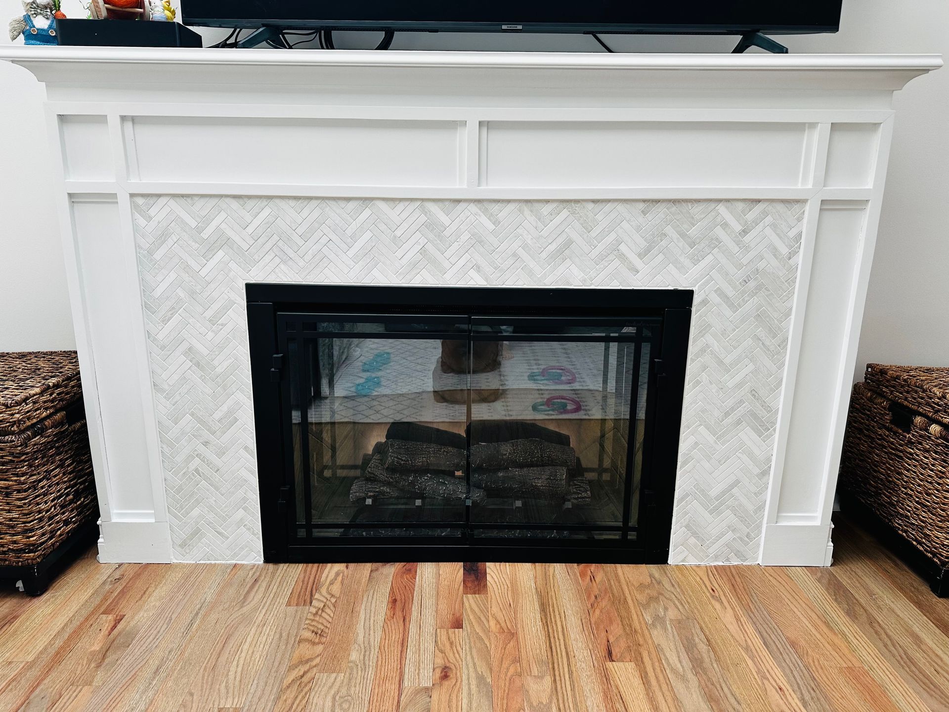 White fireplace with black glass insert and herringbone tile surround on a wood floor