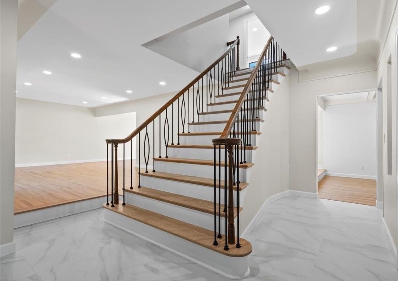 Bright foyer with a wooden staircase, black railing, and white marble tile floor