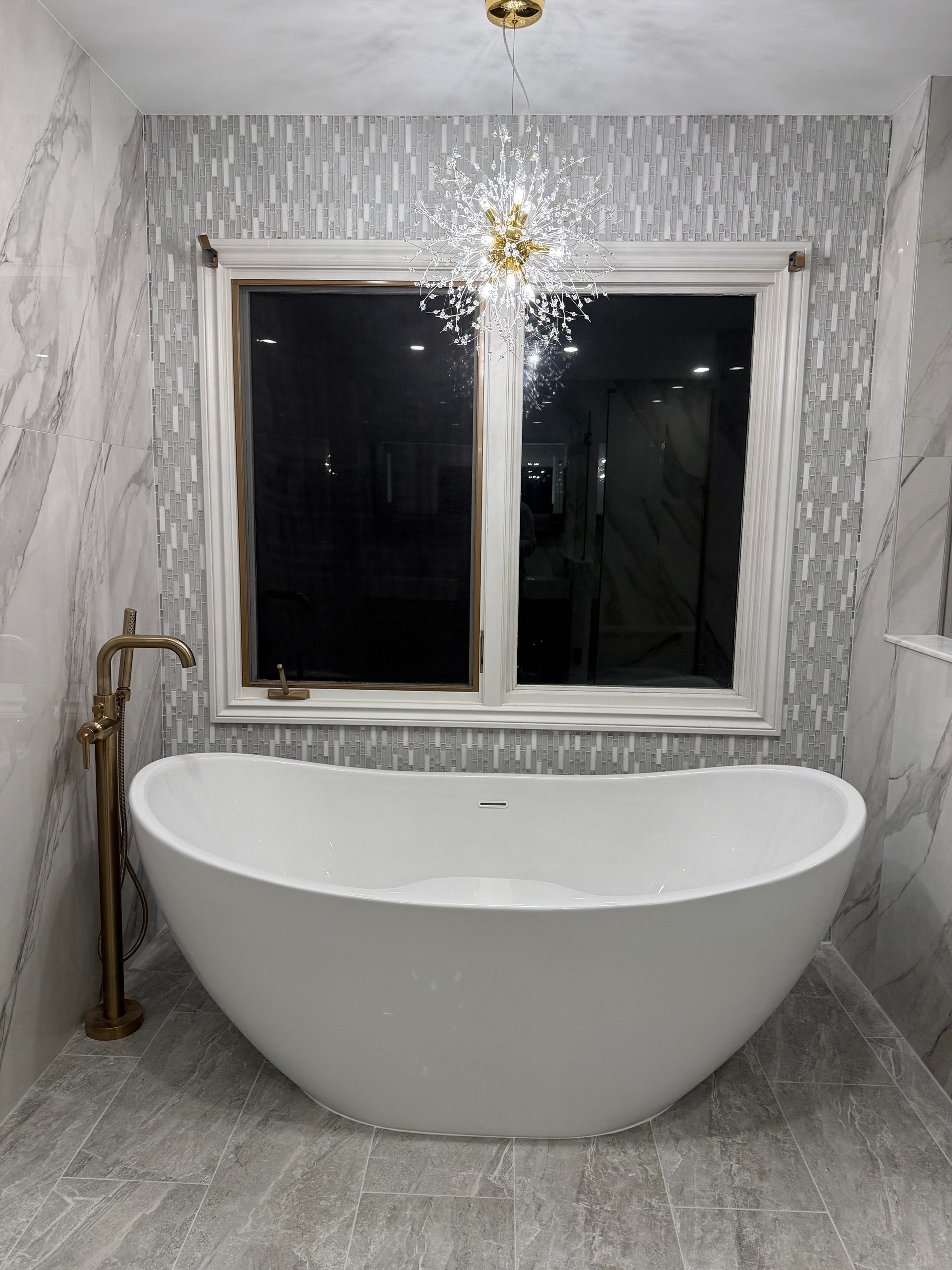 Modern bathroom with freestanding white tub, marble-pattern walls, and a window above it