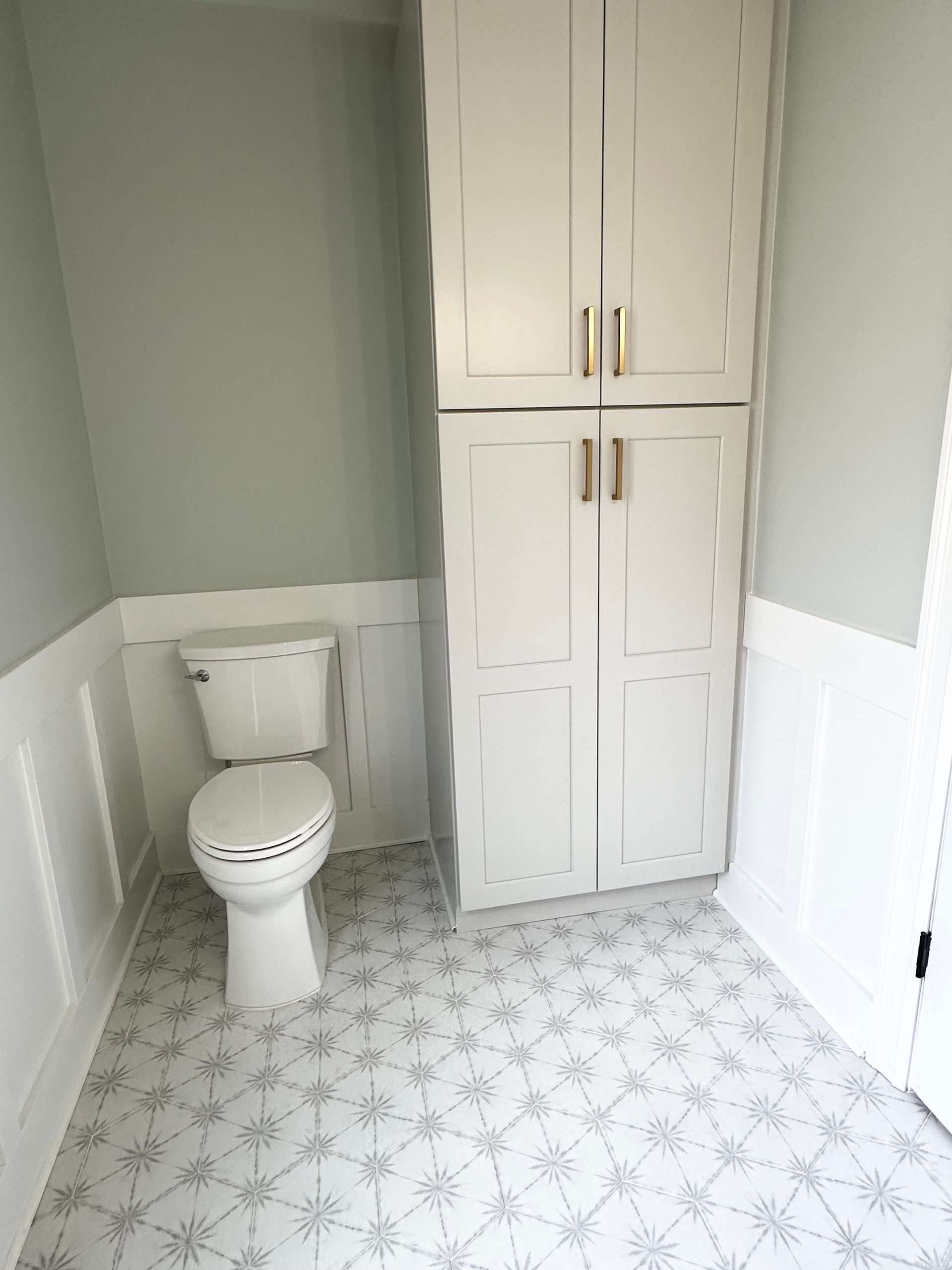 Small bathroom with a toilet, white built-in cabinets, gray walls, and patterned tile floor.