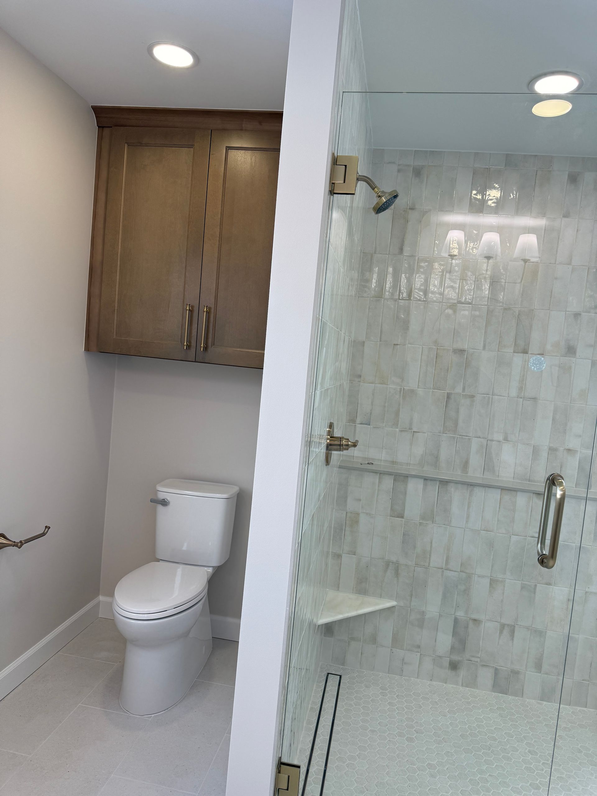 Small bathroom with white toilet, wood cabinet, and glass shower enclosure with marble tile.