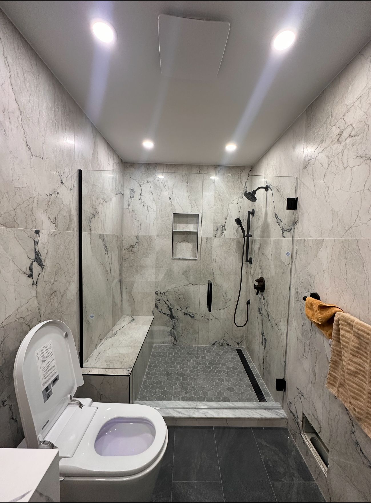 Modern bathroom with a toilet, glass shower enclosure, marble walls, and recessed ceiling lights