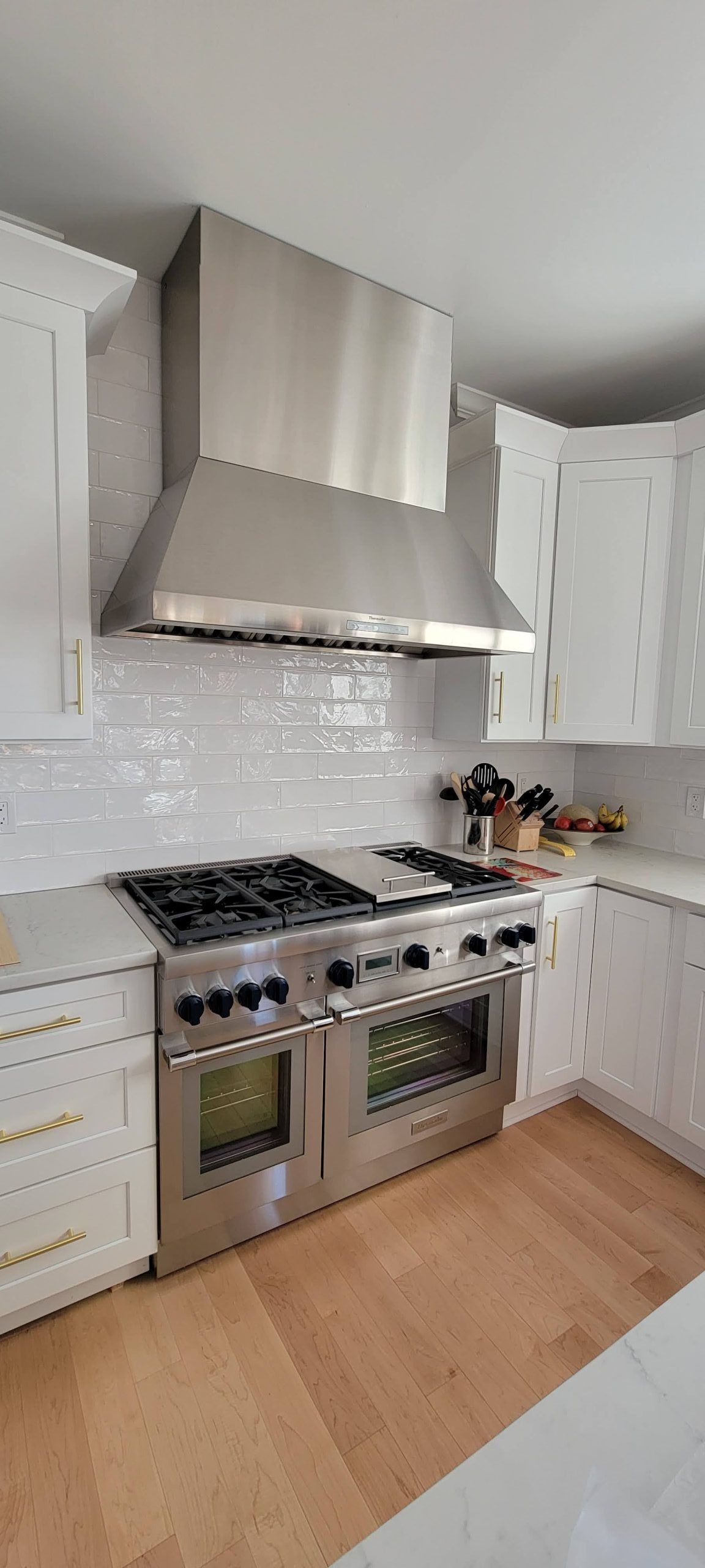 Modern white kitchen with stainless steel stove, range hood, and light wood floor