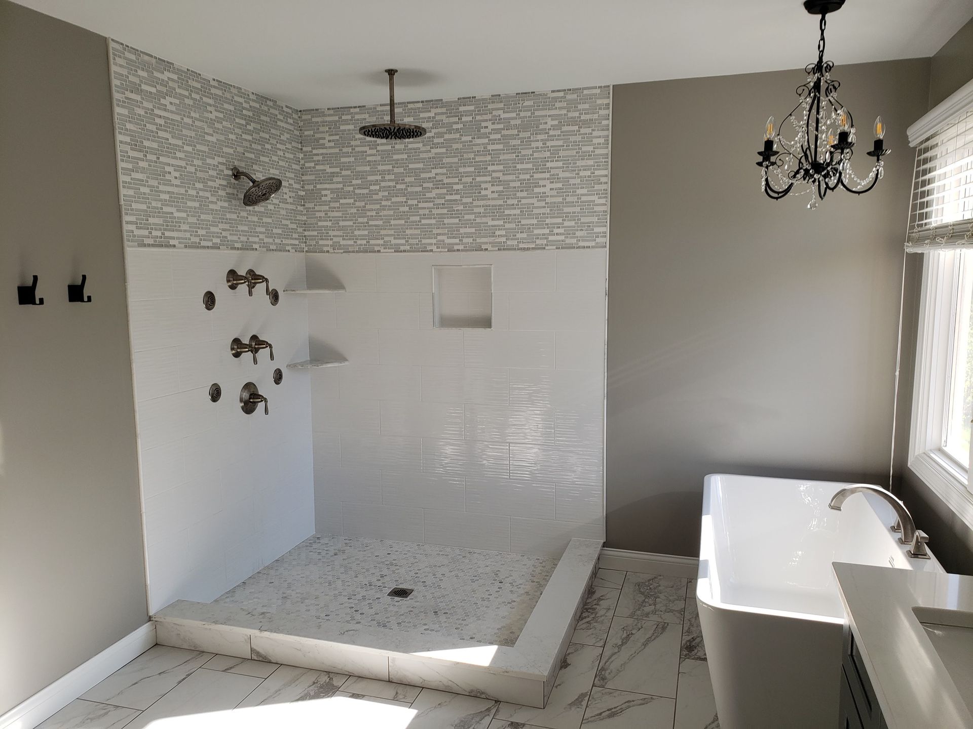 Modern bathroom with white shower, freestanding tub, chandelier, and marble-look tile floor