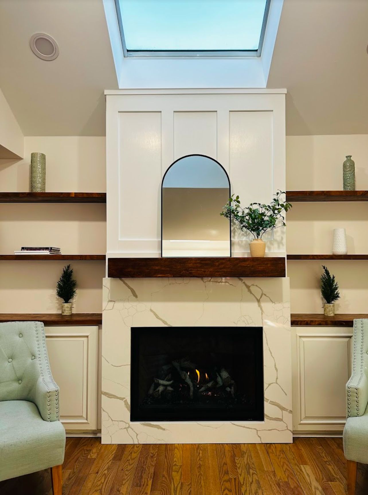 Bright living room fireplace with white built-ins, wood shelves, and skylight above.
