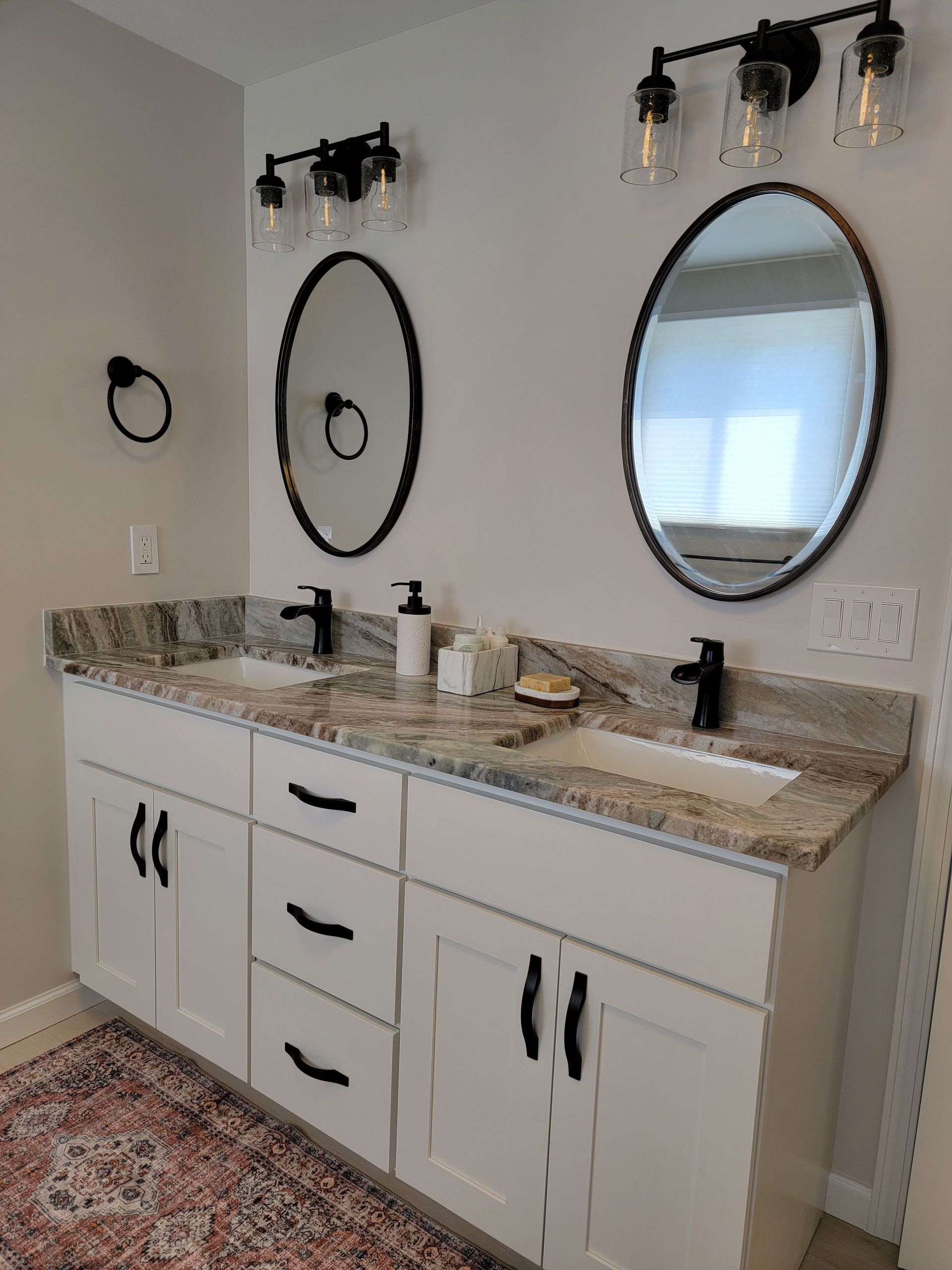 Bathroom vanity with double sinks, oval mirrors, white cabinets, and granite countertop.