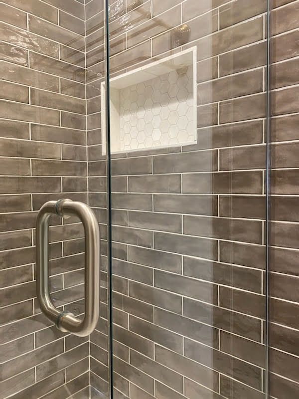 Glass shower door with brushed metal handle in a tiled bathroom