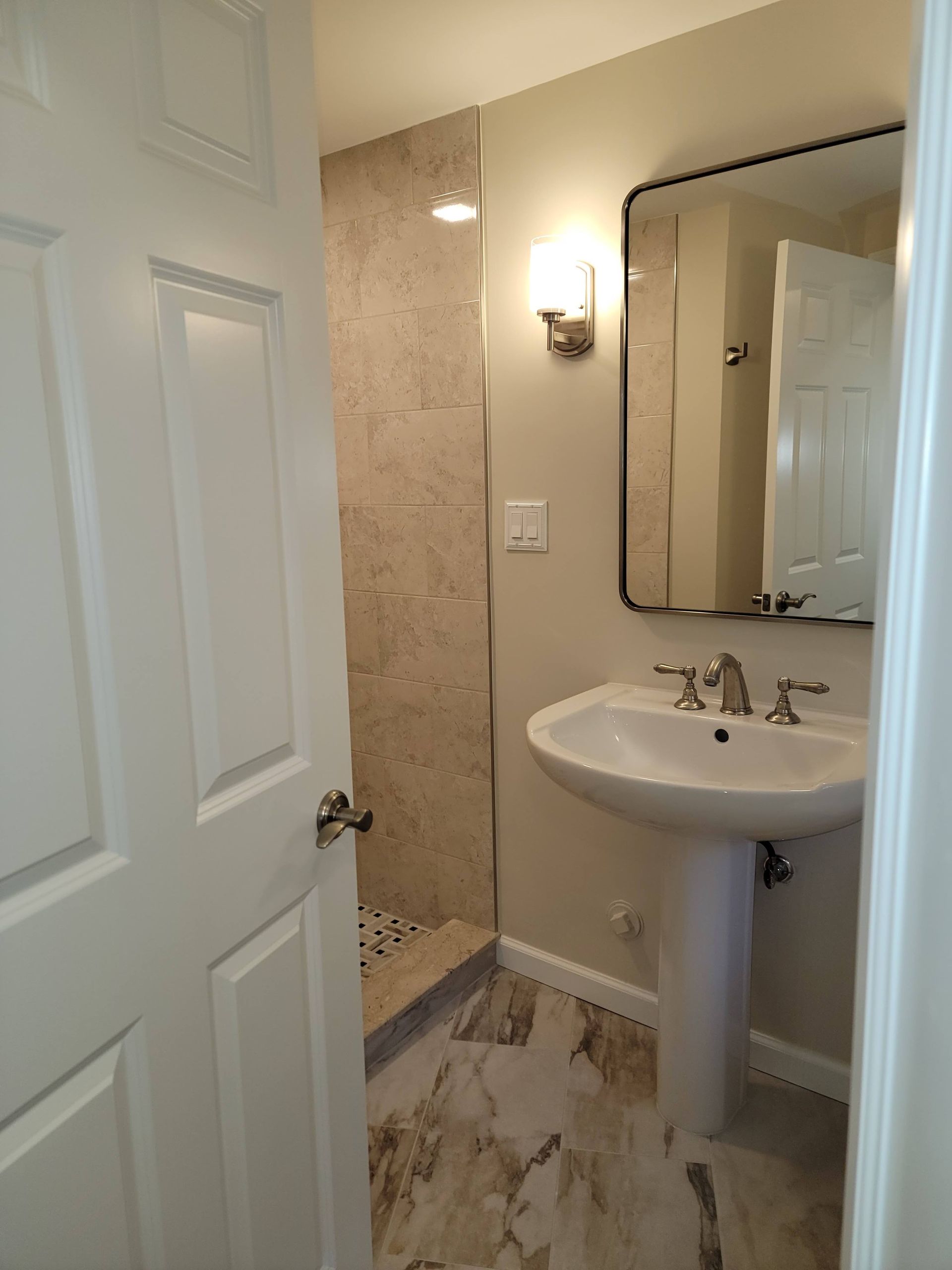Small bathroom with open door, pedestal sink, mirror, and wall sconce lighting.