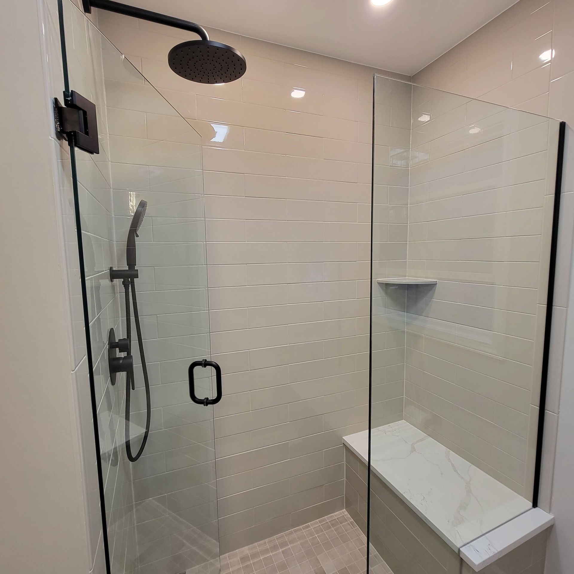 Modern glass shower with black fixtures, white tiled walls, and built-in bench in a bright bathroom