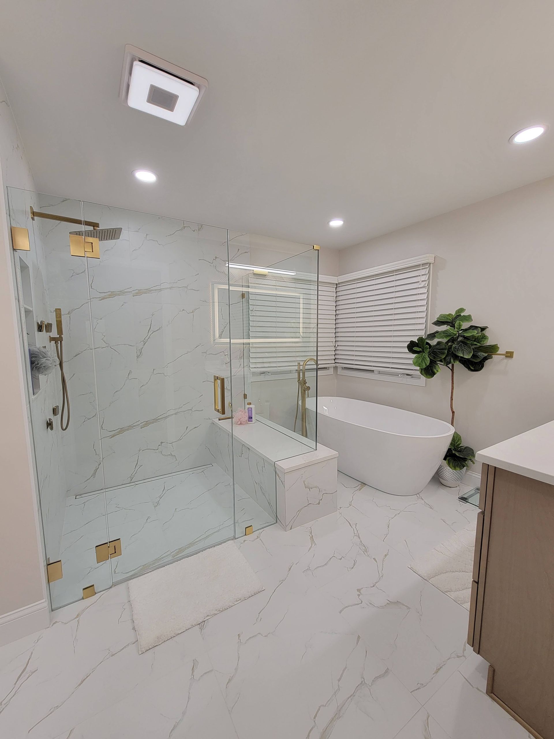 Modern bathroom with glass shower, freestanding tub, white marble floor, and recessed lighting