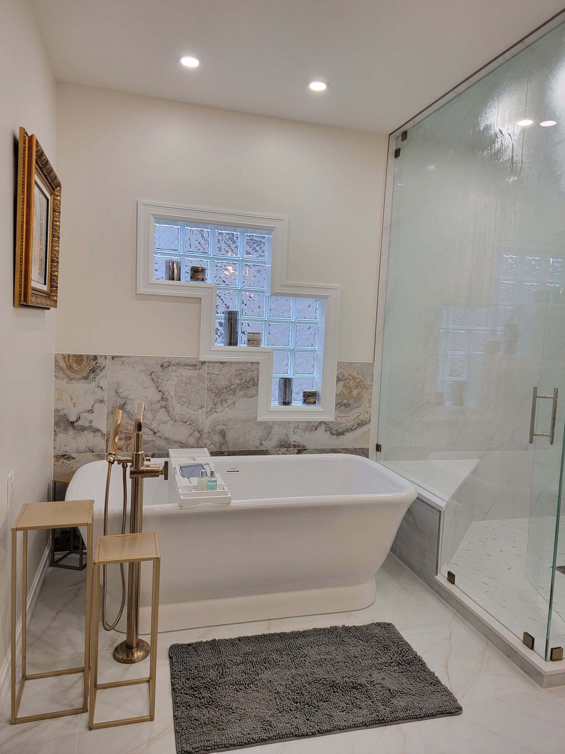 Bright modern bathroom with a freestanding tub, glass shower, marble tile, and a patterned rug.