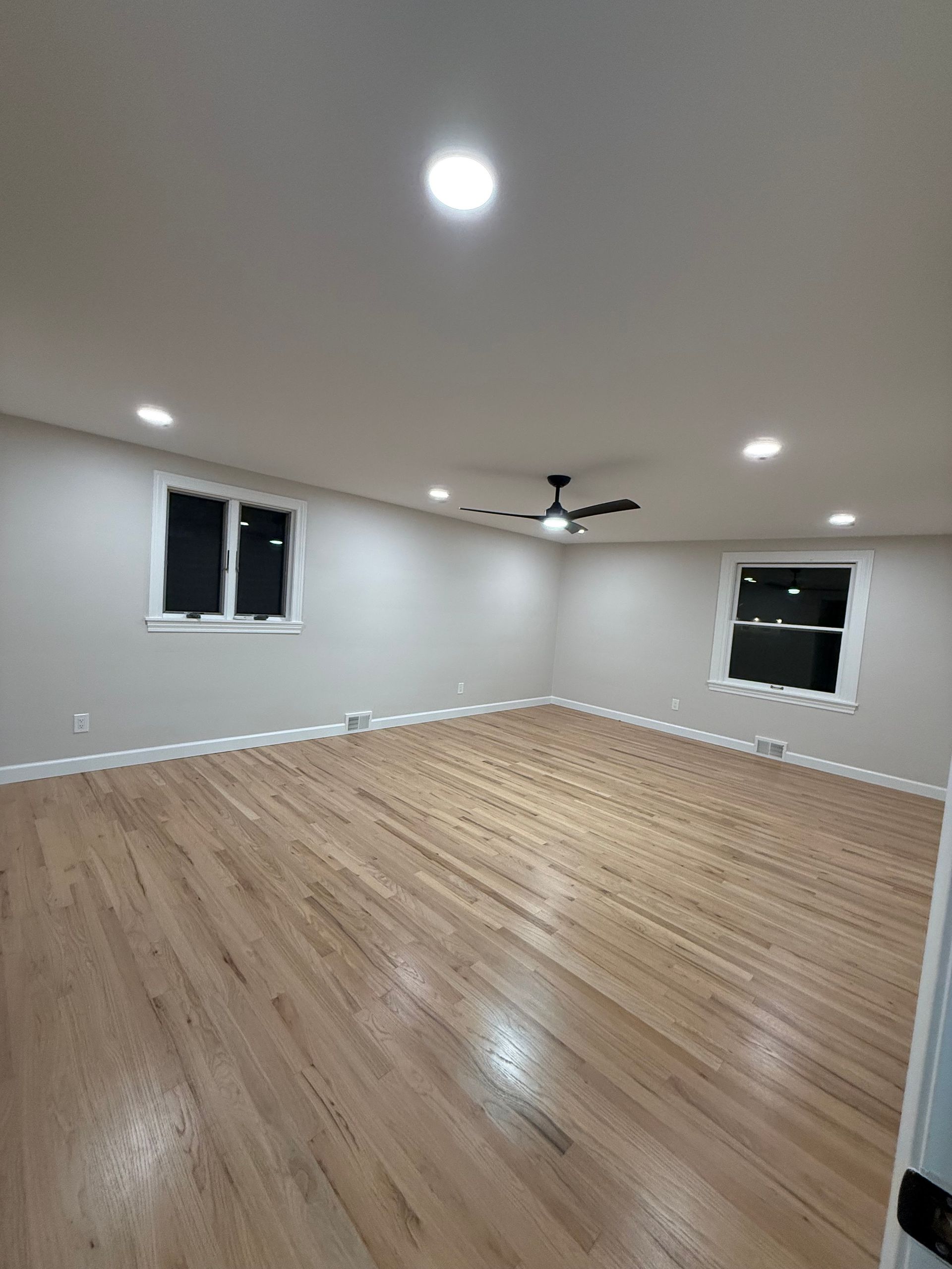 Empty unfurnished room with wood floors, white walls, recessed lights, ceiling fan, and two windows