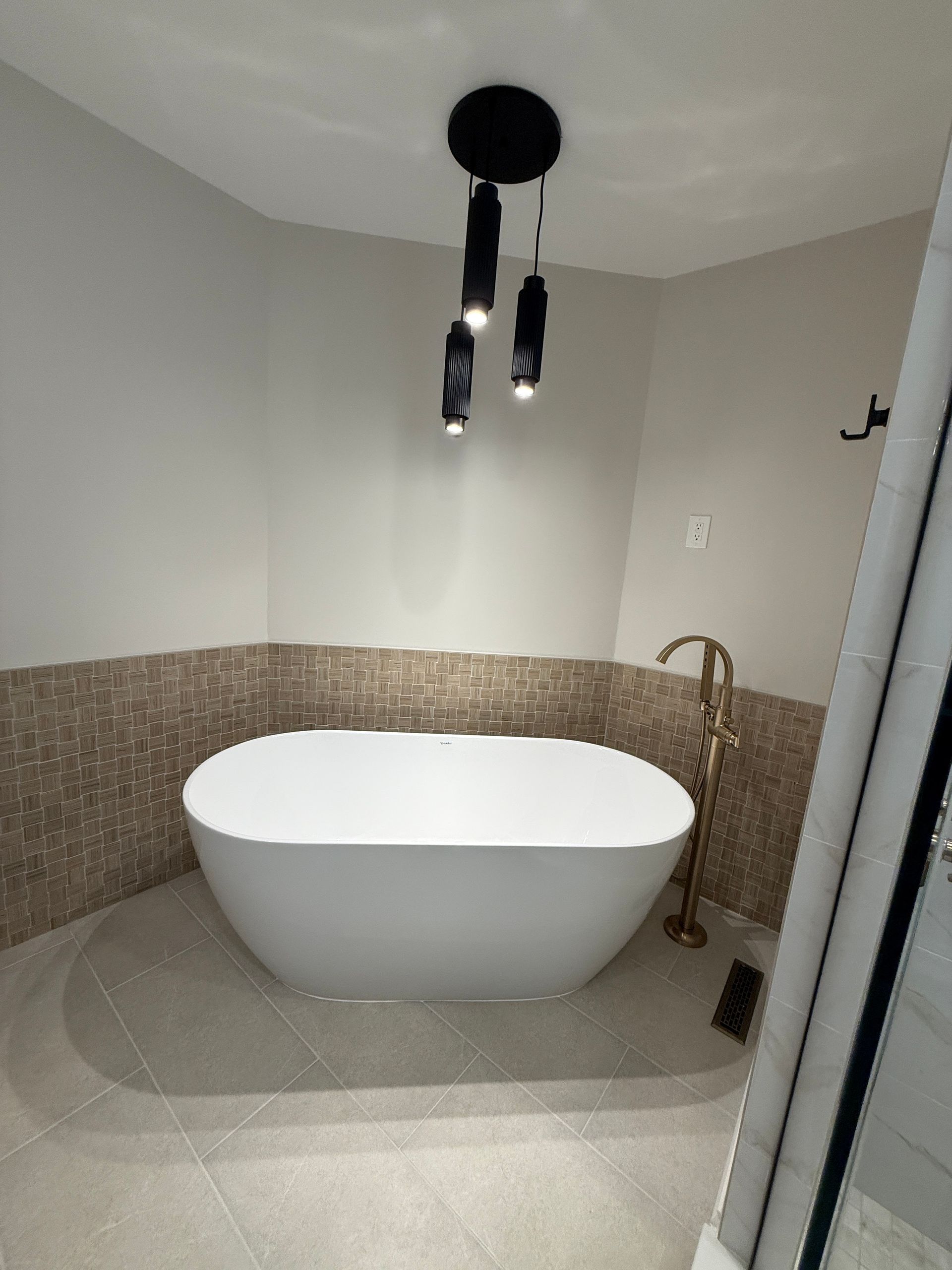 Small bathroom with a white freestanding tub, mosaic tile wall, and black ceiling light over the tub.
