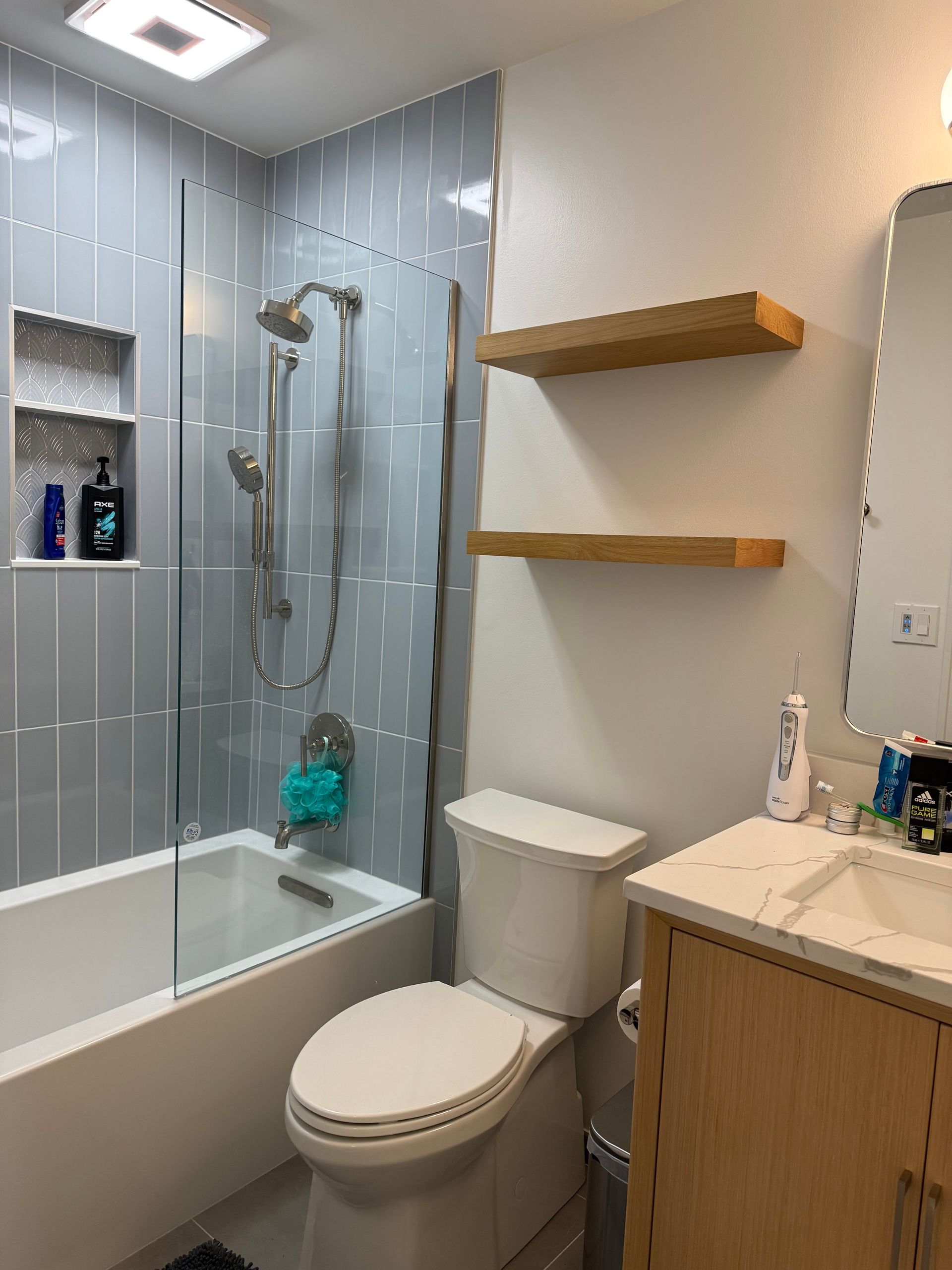 Bathroom with bathtub, glass shower, toilet, vanity sink, and wooden shelves.