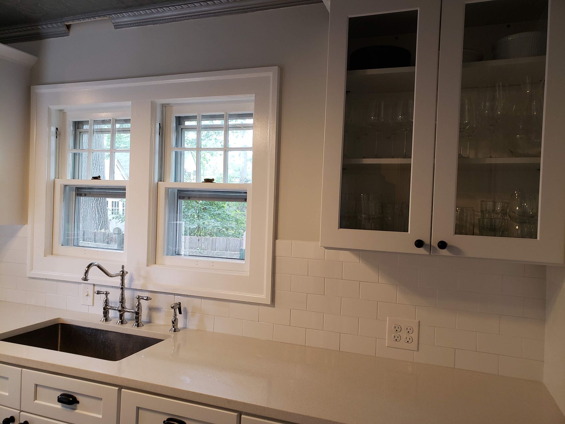 Bright kitchen with white cabinets, tiled backsplash, window over sink, and black countertop