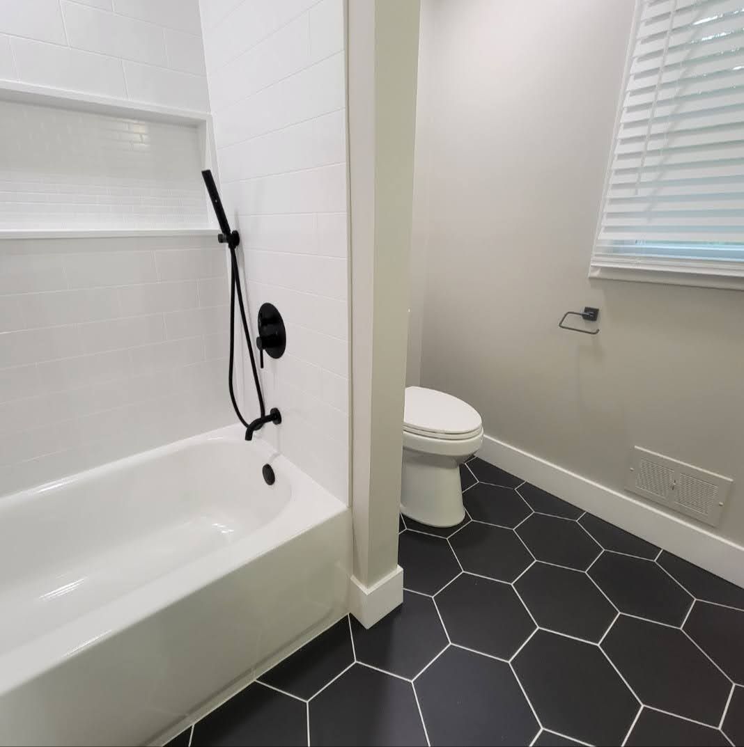 Bathroom with white tub and shower, adjoining toilet area, and dark hexagonal tile floor