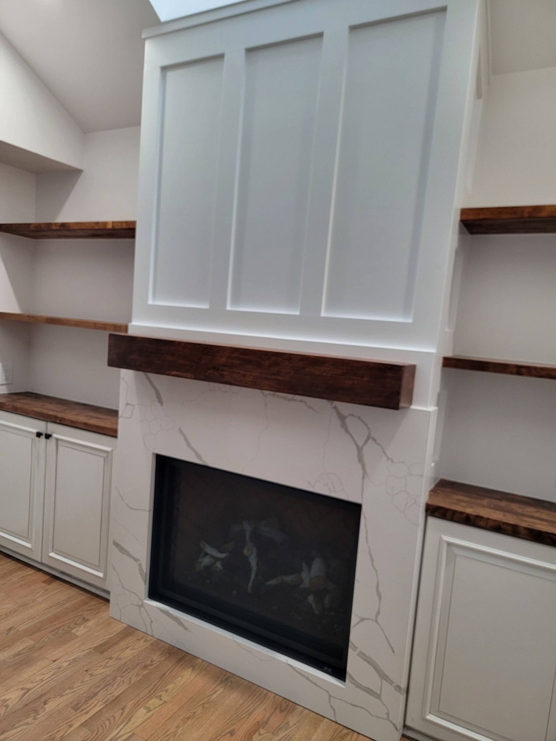 Built-in white fireplace with marble surround and wood shelves in a bright room