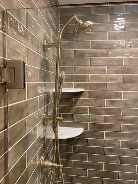 Accessible shower with grab bars, bench, and brass showerhead in a tiled bathroom.