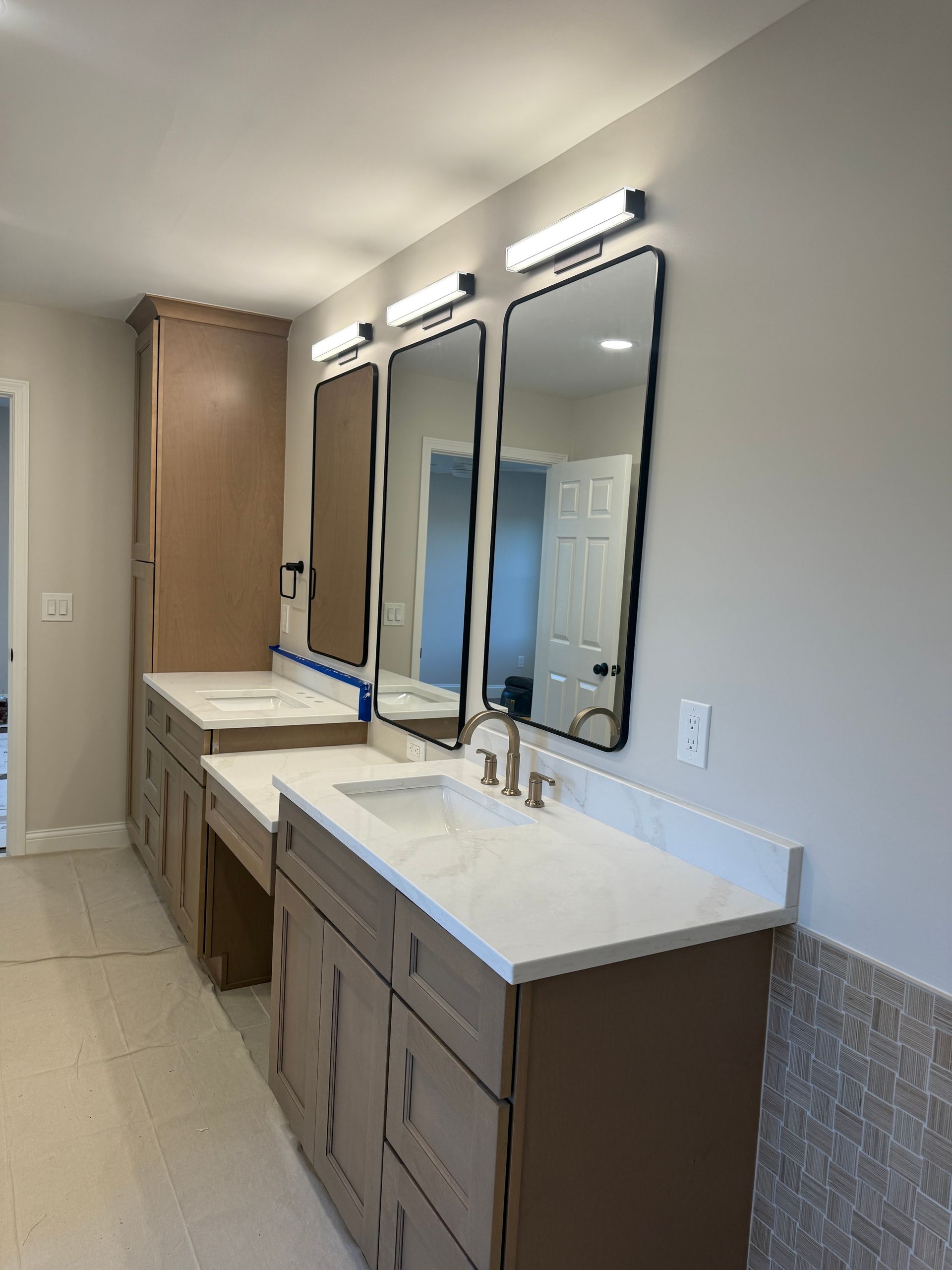 Bathroom with long vanity, two mirrors, sinks, wall lights, and wood cabinets.