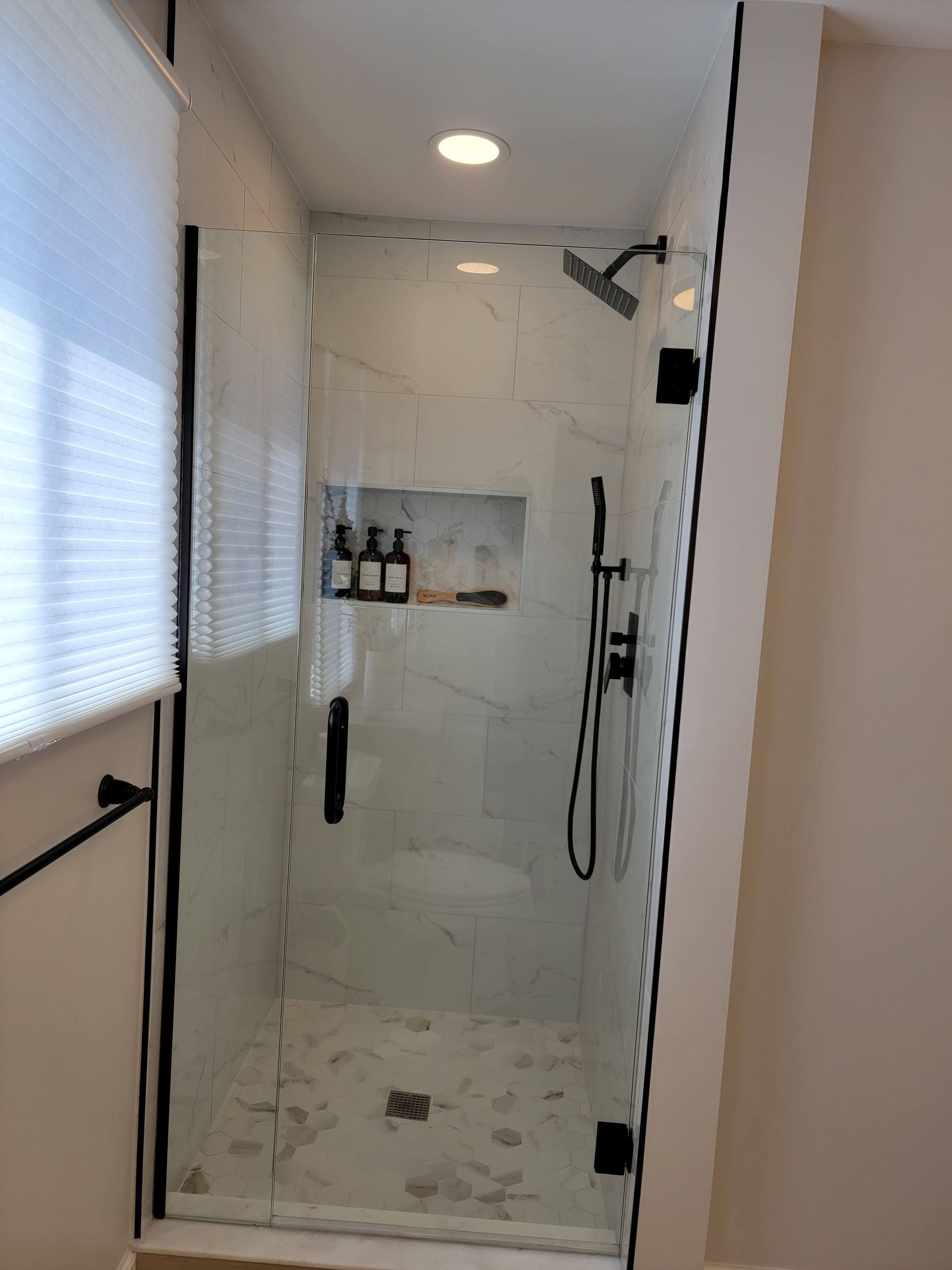 White tiled shower with black fixtures, built-in shelf, and wall-mounted showerhead in a narrow bathroom.