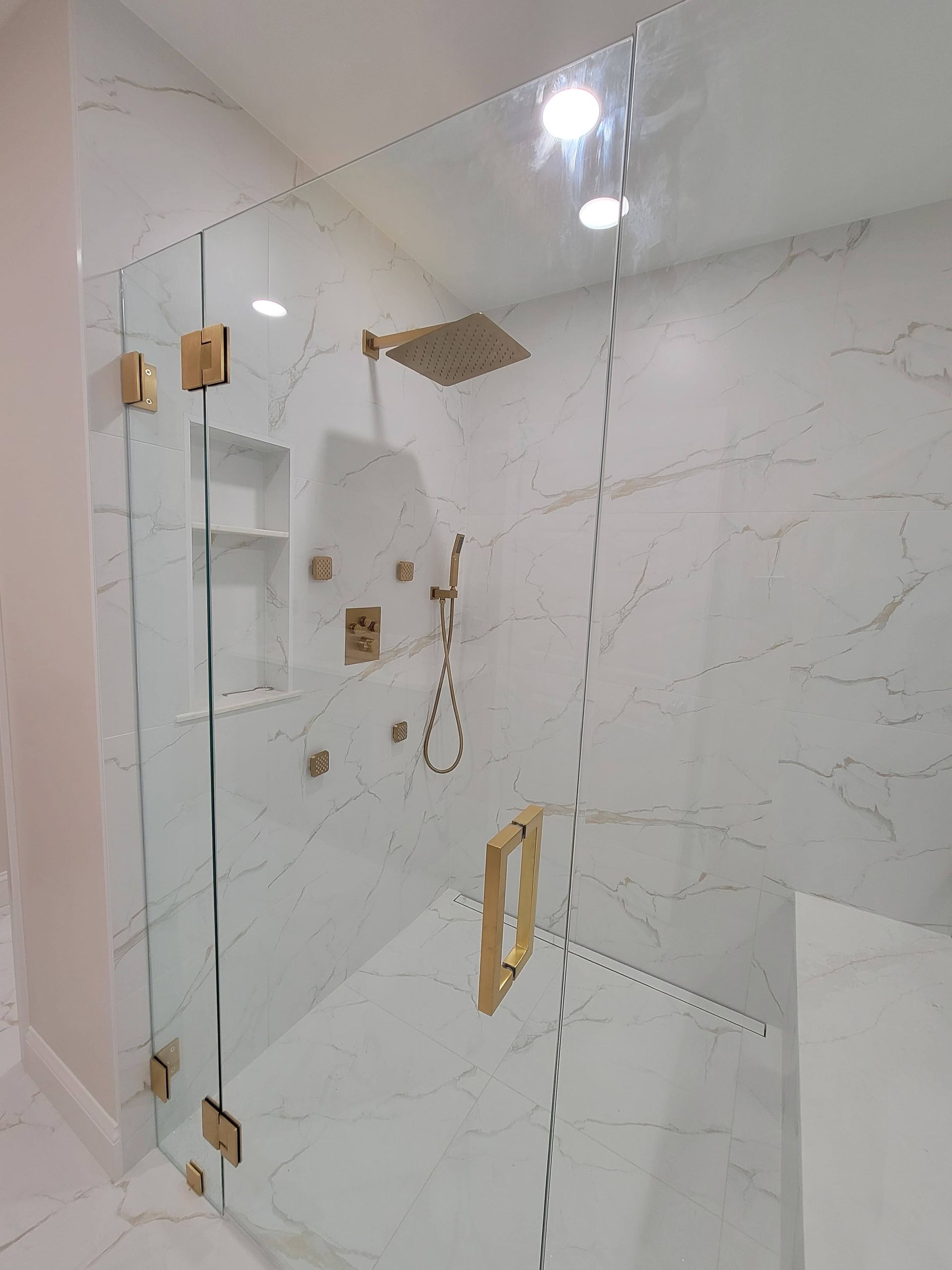 Glass shower enclosure in a tiled bathroom with gold hardware and a handheld shower head