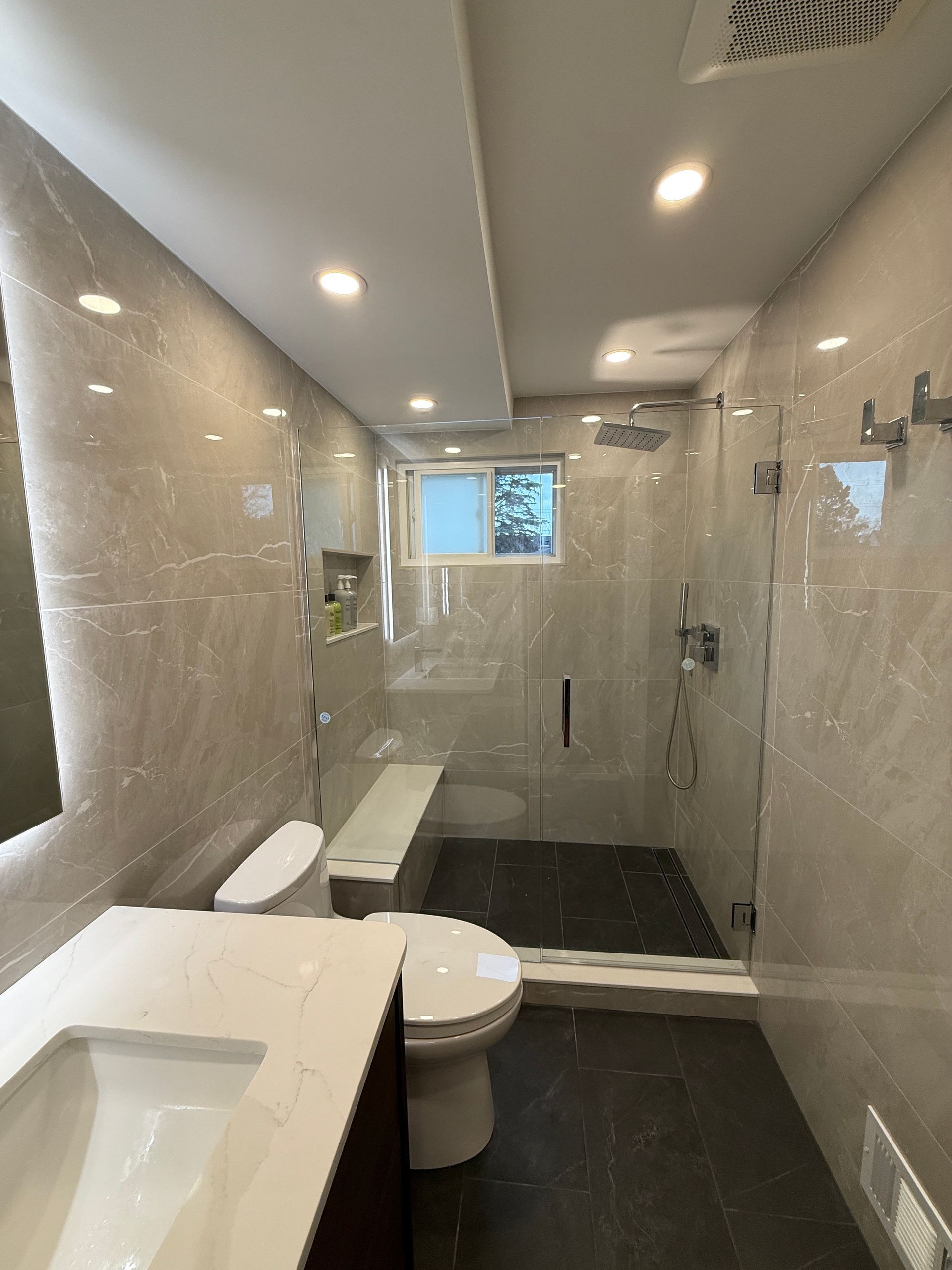 Modern bathroom with glass shower, toilet, sink, and beige tiled walls