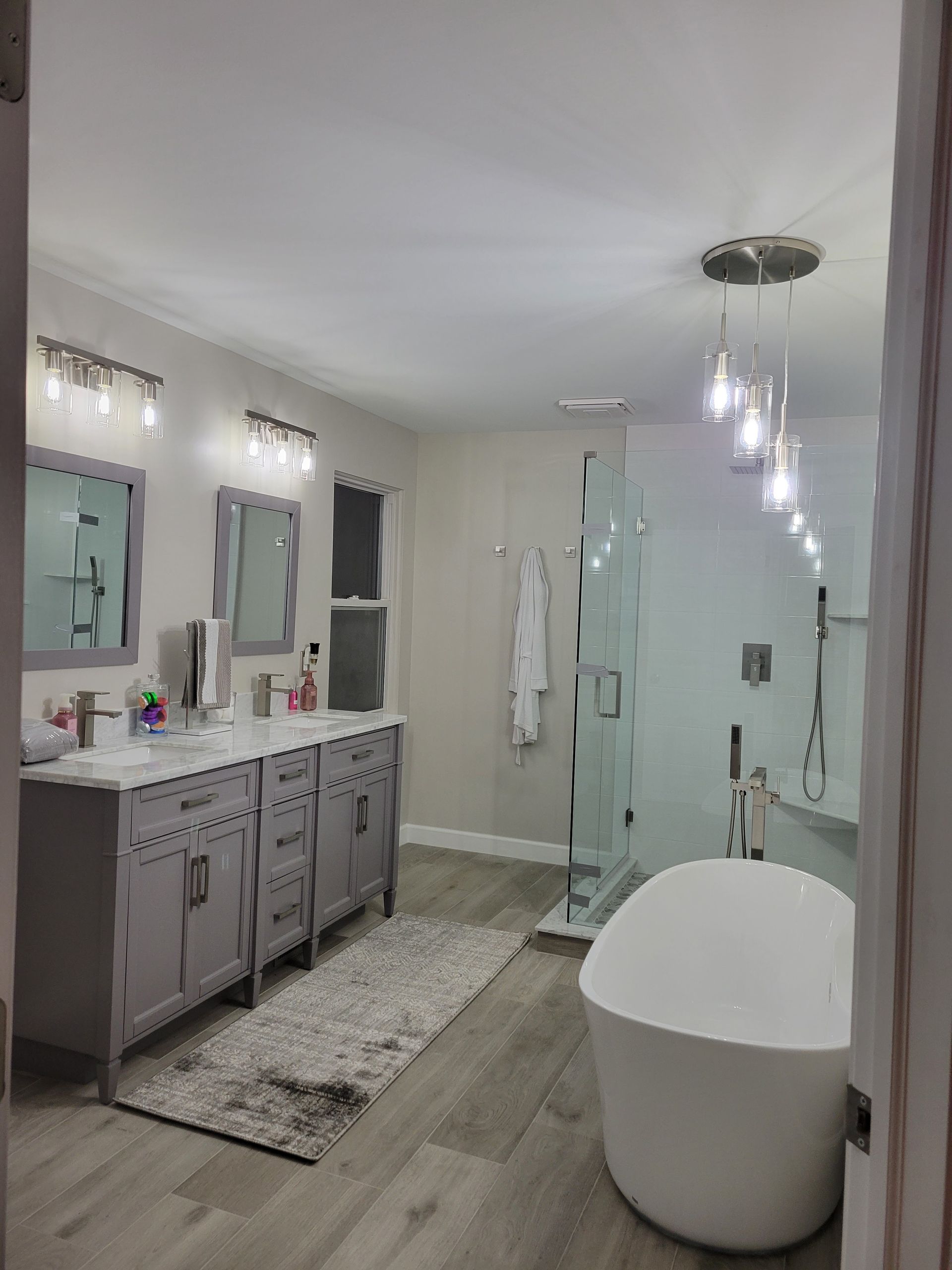 Modern bathroom with double vanity, mirrors, glass shower, and freestanding tub under soft lighting