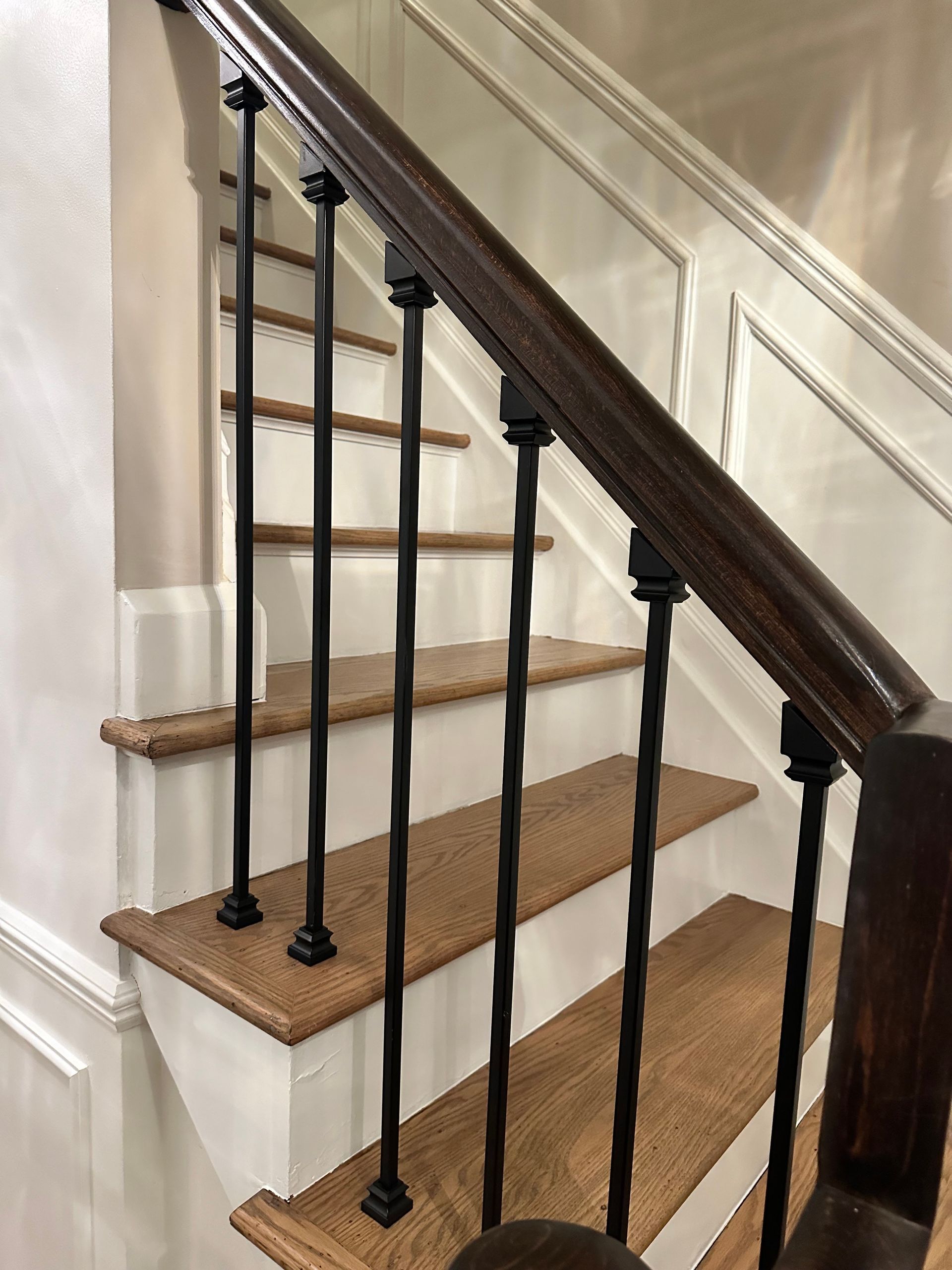 Carpeted staircase with black metal balusters and dark wood handrail in a beige interior