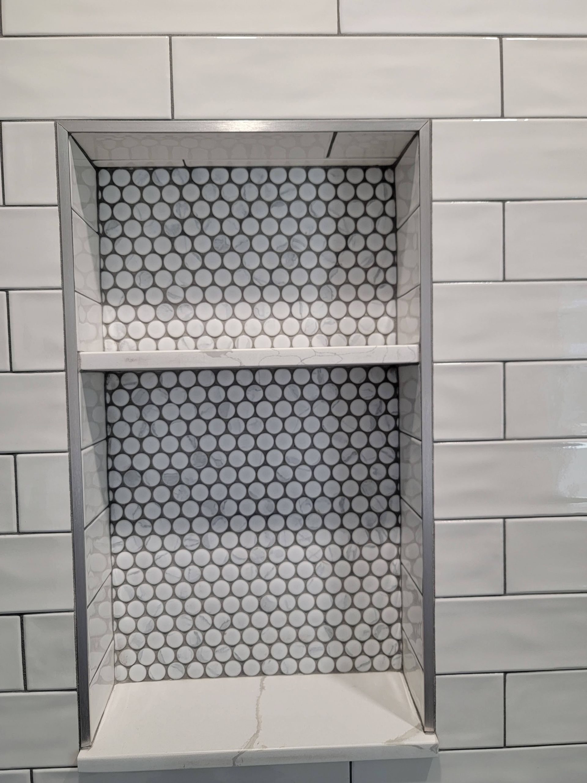 Tiled wall niche with white hexagonal mosaic backing and gray marble-style frame