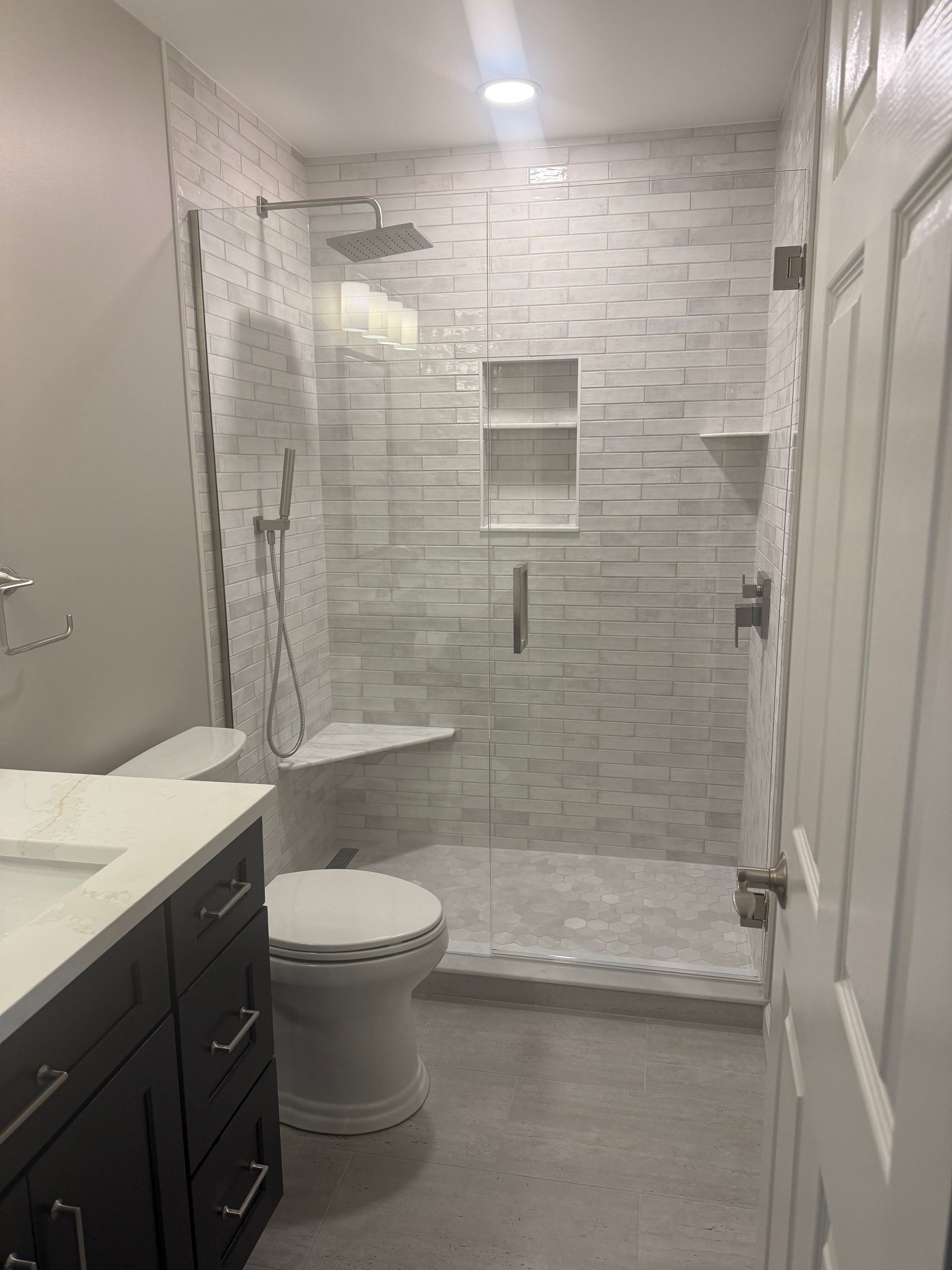Modern bathroom with white tile shower, glass door, gray floor, vanity, and toilet