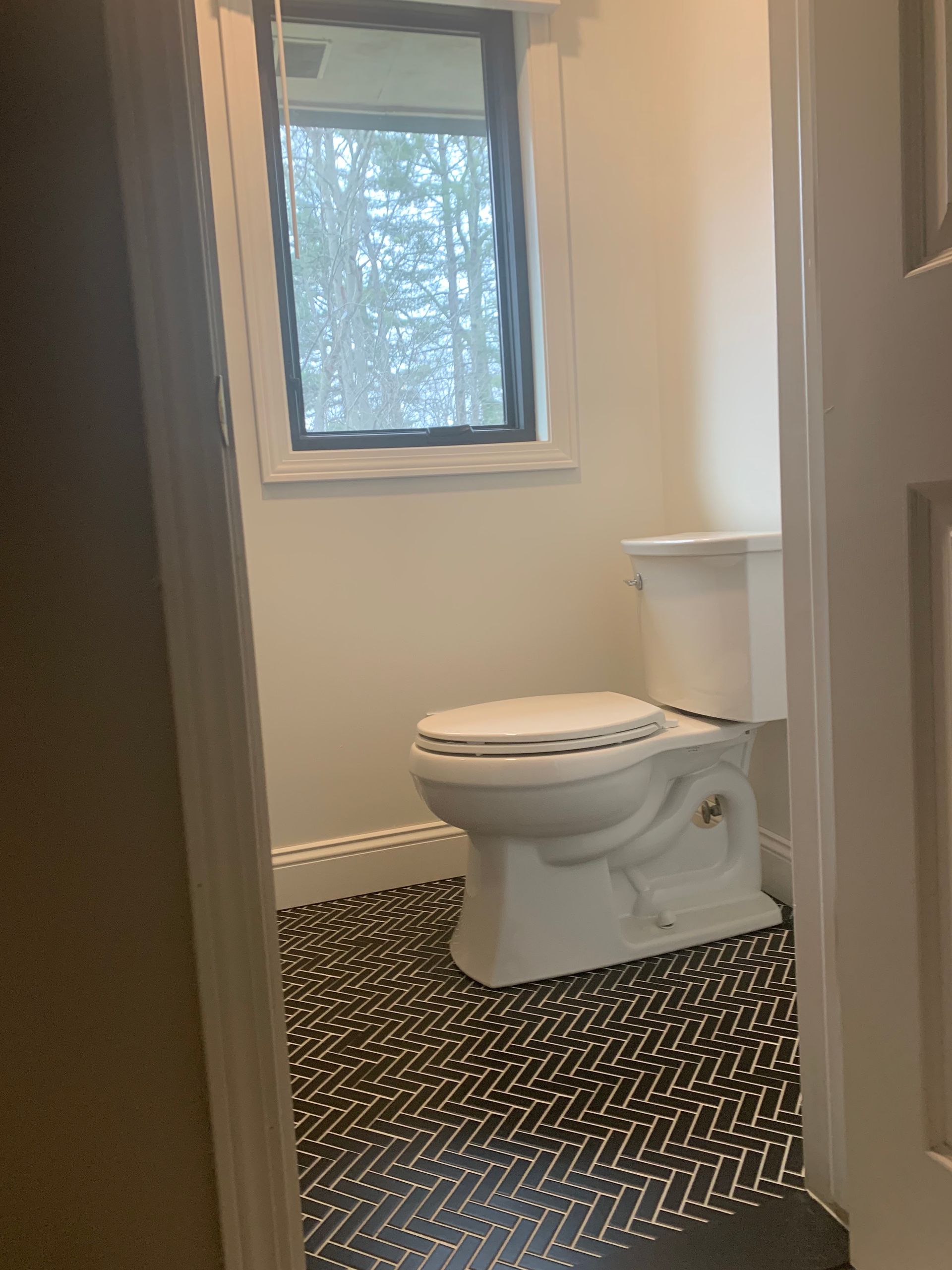Small bathroom with a white toilet, window, and black patterned floor tiles.