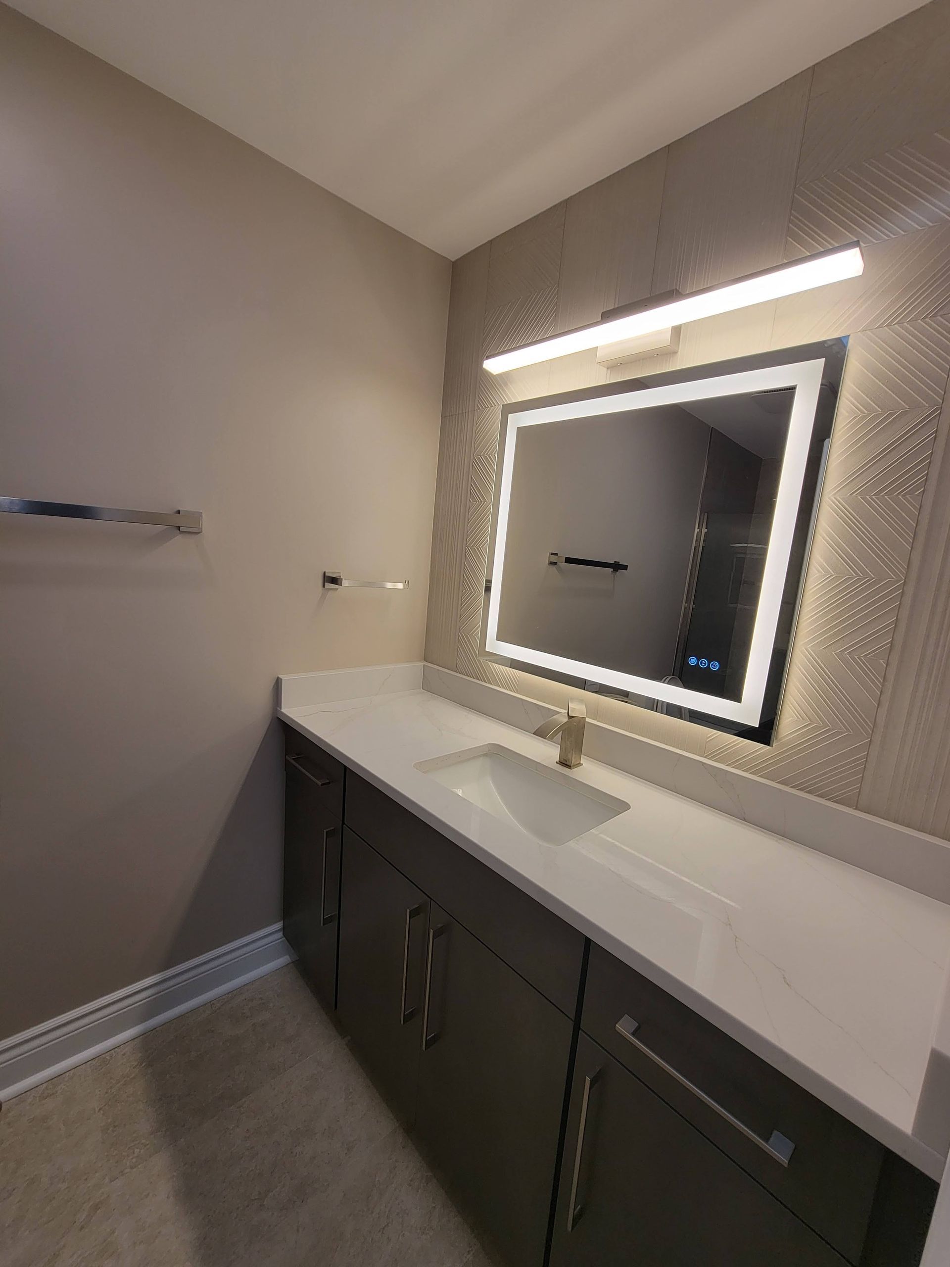 Modern bathroom vanity with illuminated mirror, white countertop, and dark cabinets
