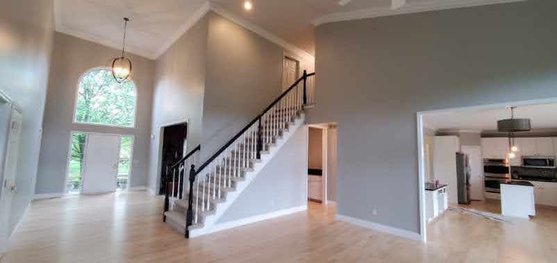 Bright open foyer with high ceilings, staircase, arched window, and view into a kitchen and dining area.